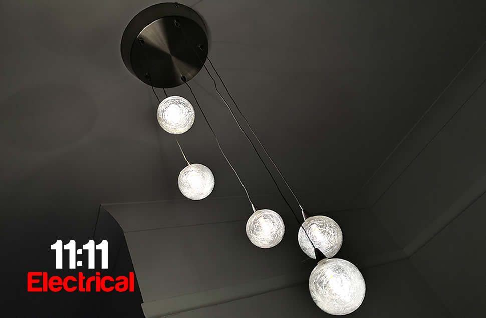 Photo of a hallway hanging light at the top of stairs, 5 cracked clear balls with warm lamps hanging at different heights